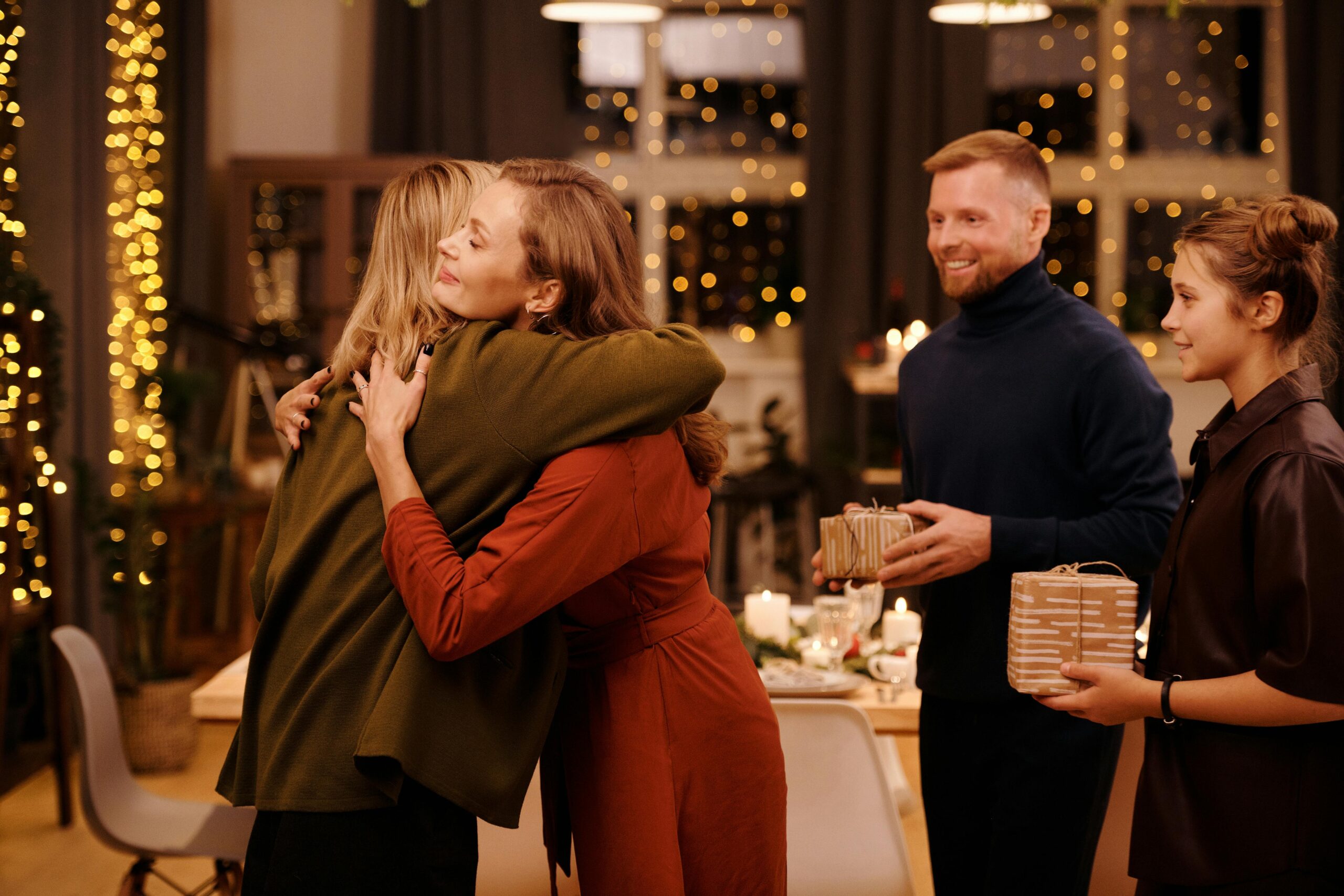 familia-que-se-estan-dando-los-regalos-de-navidad-dos-mujeres-se-abrazan-como-muestra-de-agradecimiento-y-otras-dos-personas-estan-esperando-a-dar-sus-regalos